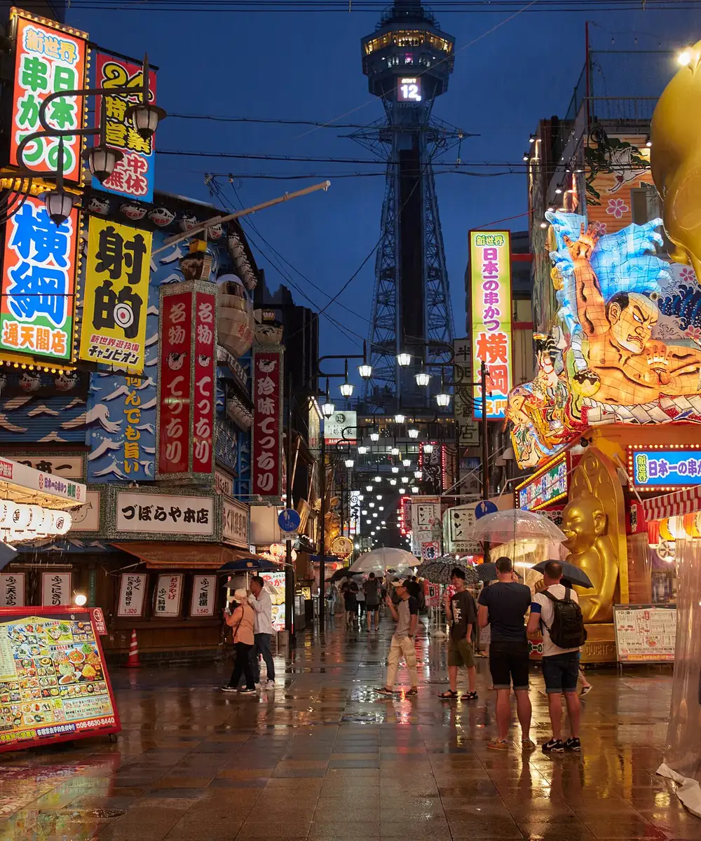 Calle de Shinsekai al anochecer, con carteles encendidos y la torre Tsutenkaku al fondo